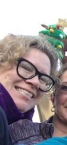 A smiling woman with curly hair and glasses wears a small Christmas tree headband.