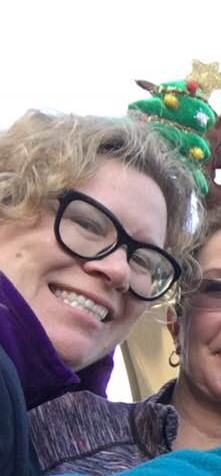 A smiling woman with curly hair and glasses wears a small Christmas tree headband.
