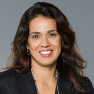 A smiling woman with long, dark hair and a black blazer looks directly at the camera.