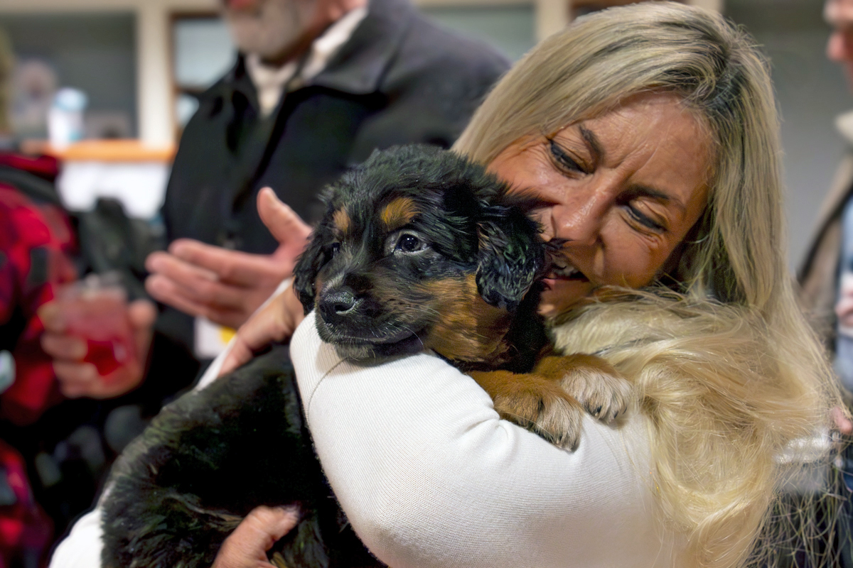 A woman closely hugs a black-and-tan puppy at an indoor gathering