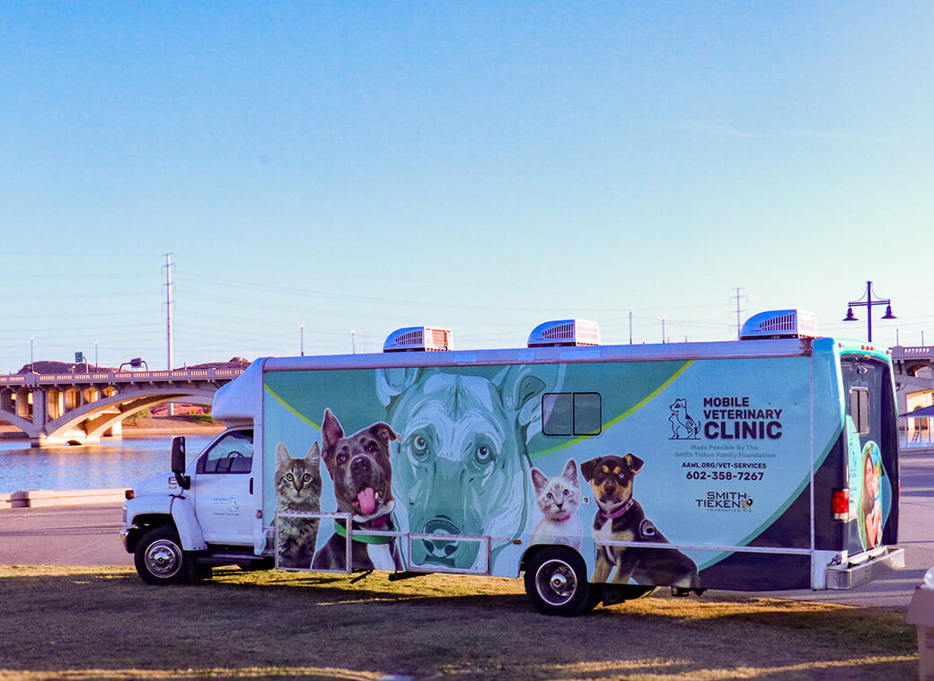 La clínica veterinaria móvil de AAWL estacionada junto al lago, decorada con ilustraciones de perros y gatos