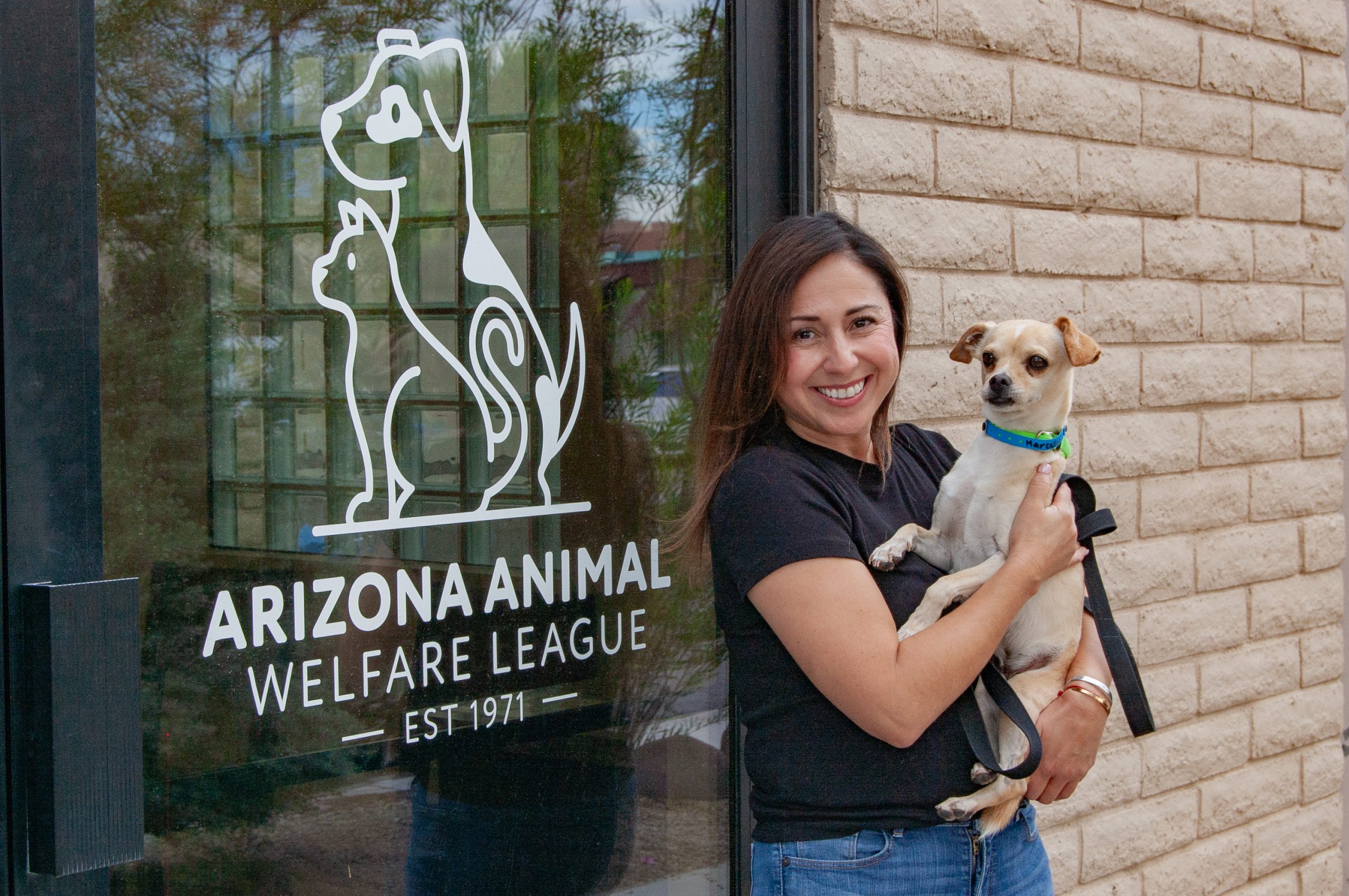 Una mujer sostiene a un perro pequeño color canela junto al letrero de Arizona Animal Welfare League en la entrada
