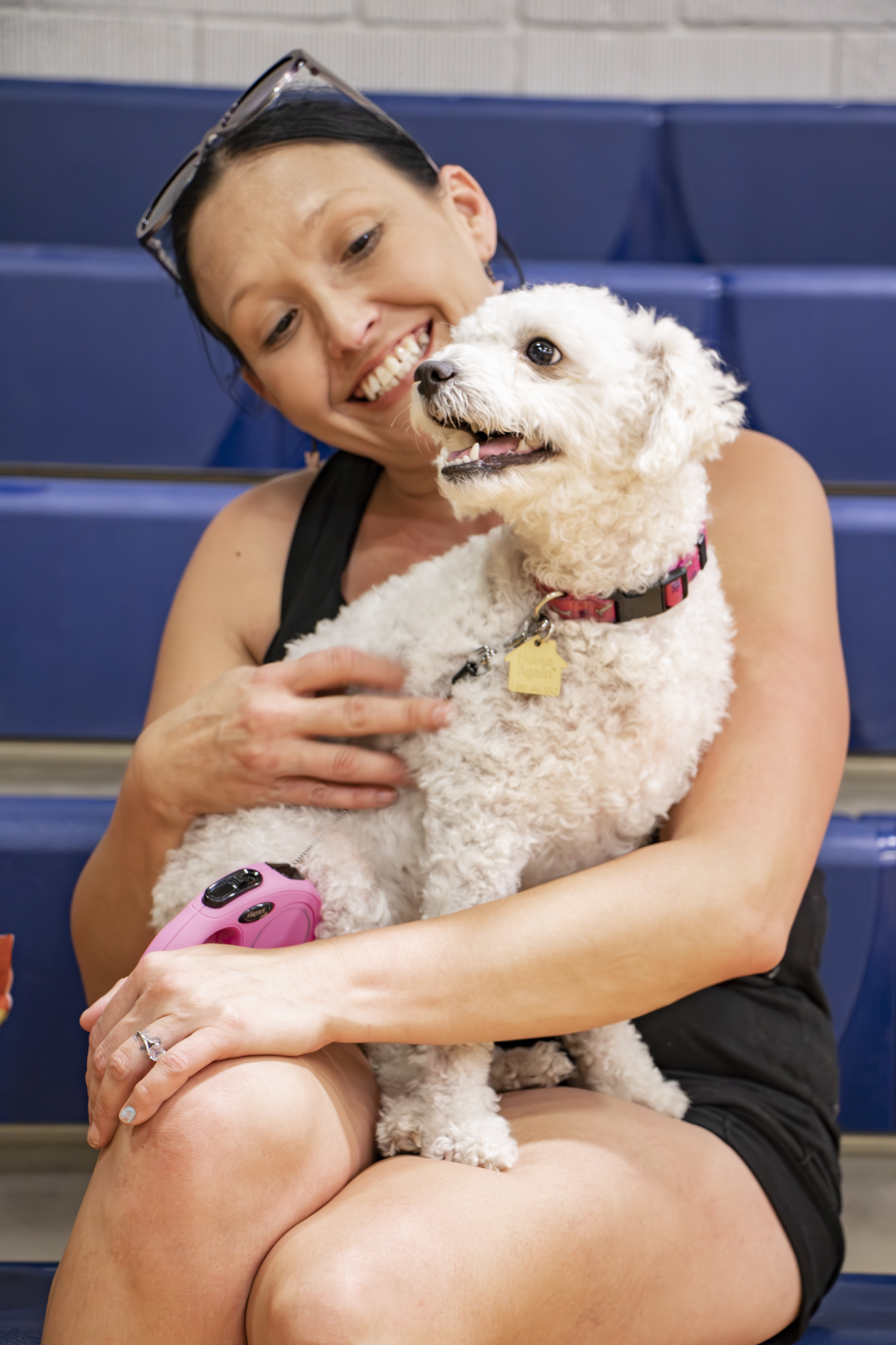 A smiling woman holds a small white curly-coated dog close against her cheek